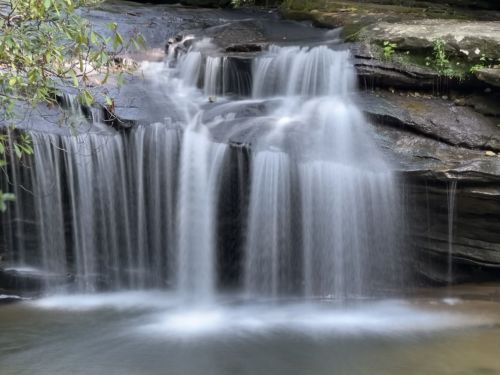 A serene waterfall cascading over smooth rocks into a calm pool, surrounded by lush greenery.