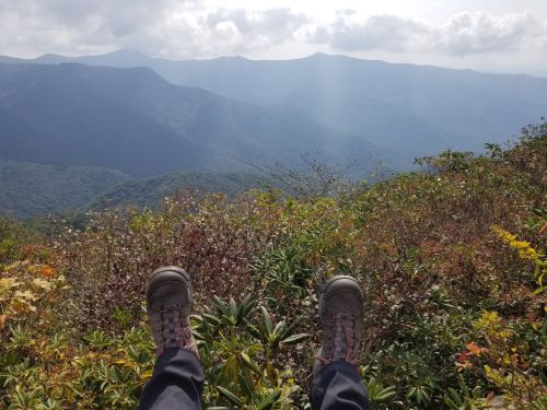 A pair of hiking boots resting on a colorful hillside, overlooking a vast mountain landscape under a cloudy sky.