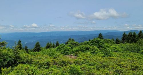 A panoramic view of lush green mountains under a blue sky with scattered clouds.