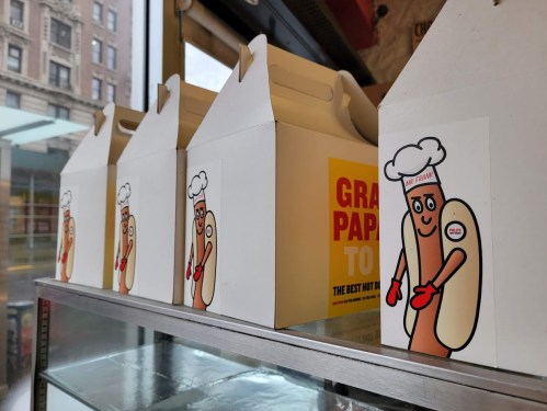 A row of white takeout boxes featuring a cartoon hot dog character with a chef's hat and red gloves.