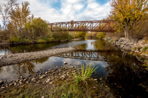 A tranquil river scene with a bridge, surrounded by autumn trees and rocky banks, reflecting in the water.
