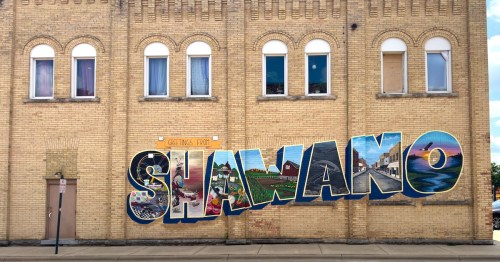 A colorful mural reading "Greetings from Shawano" on a city street in Wisconsin.