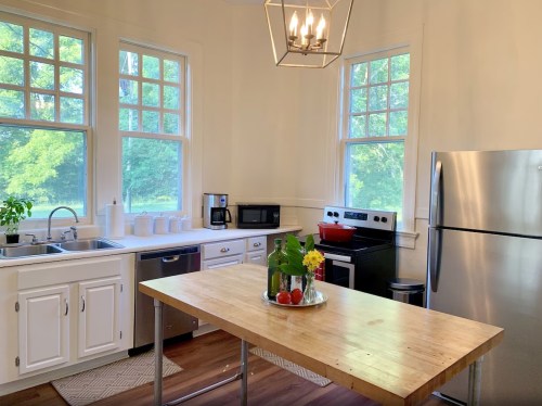 Bright kitchen with large windows, stainless steel appliances, a wooden table, and fresh flowers on display.