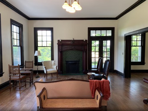 A spacious room with vintage furniture, a fireplace, and large windows, featuring a cozy atmosphere and wooden accents.