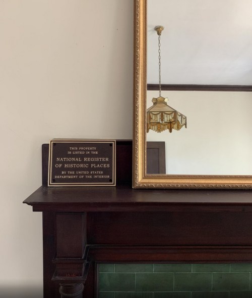 A vintage mirror above a mantel, with a sign indicating the property is on the National Register of Historic Places.