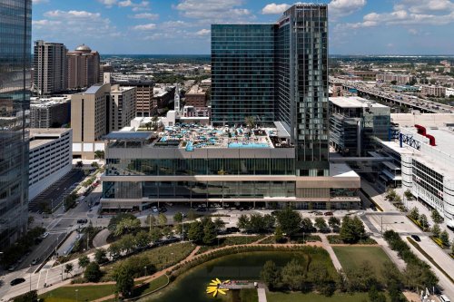 Aerial view of a modern urban area featuring a high-rise building with a rooftop pool and surrounding greenery.