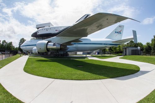 NASA's modified Boeing 747 with a space shuttle mounted on top, displayed on a grassy area with a walkway.