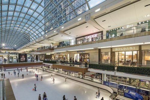 A spacious shopping mall with a glass ceiling, featuring an ice skating rink and various luxury stores.
