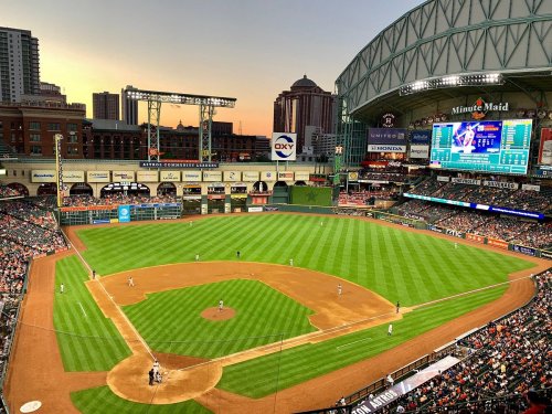 Aerial view of a baseball game at Minute Maid Park during sunset, with players on the field and fans in the stands.