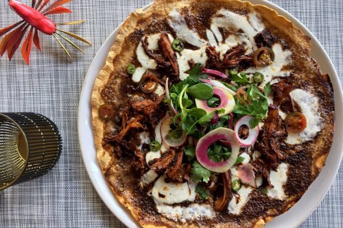 A colorful plate of shredded meat on a tortilla, topped with onions, cilantro, and drizzled with sauce.