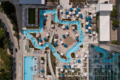 Aerial view of a Texas-shaped pool area with lounge chairs, umbrellas, and surrounding greenery.