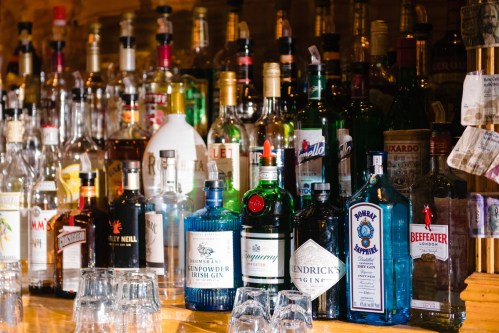 A variety of colorful liquor bottles displayed on a bar shelf, with glasses in the foreground.