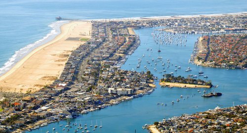 Aerial view of a coastal area with a sandy beach, marina, and boats along a winding waterway.