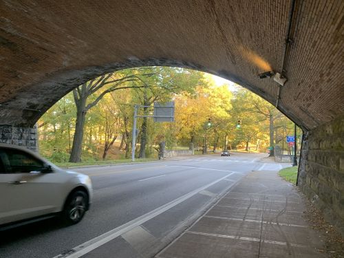 A view from under a brick archway, showing a road with a car and trees in vibrant autumn colors.