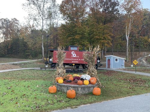 A vintage train car near a pumpkin display, surrounded by autumn trees and a small building in the background.