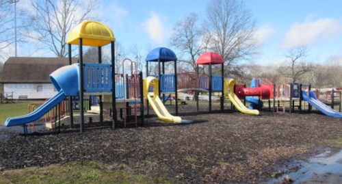 Colorful playground equipment with slides, set in a grassy area under a blue sky with scattered clouds.