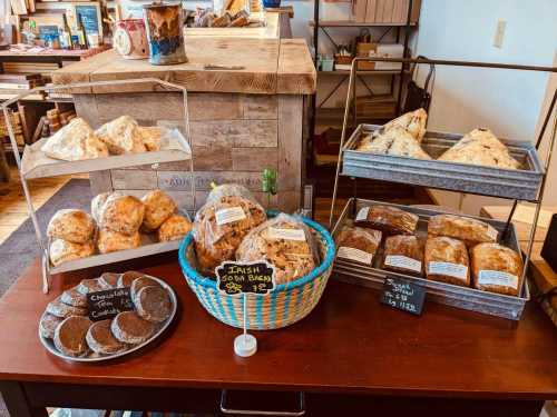 A display of baked goods including scones, cookies, and bread, arranged on wooden tables and metal trays.