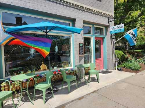 A colorful bakery exterior with outdoor seating, a rainbow flag, and an "Open" sign on a sunny day.