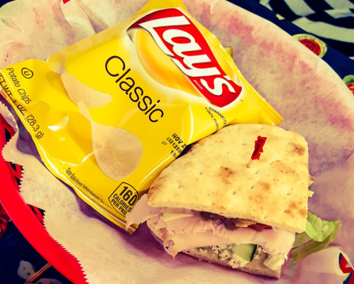 A sandwich with turkey and vegetables on a plate, accompanied by a bag of Lay's Classic potato chips.