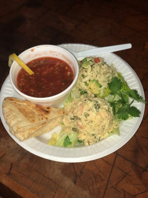 A plate with salad, hummus, pita bread, and a cup of salsa on a wooden table.