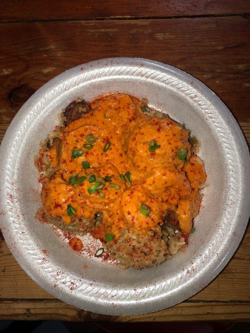 A plate of spicy shrimp topped with a creamy sauce and green onions, served over a bed of rice.