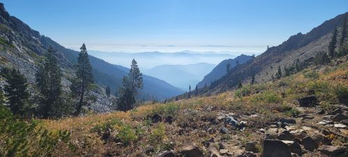 A scenic mountain landscape with rolling hills, trees, and a misty blue horizon under a clear sky.