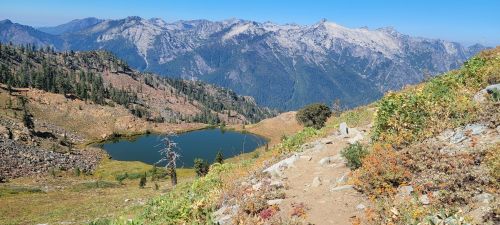 A scenic mountain landscape featuring a clear lake surrounded by rocky terrain and lush greenery under a blue sky.