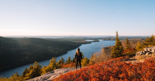Hiker stands at the top of a rocky overlook in Acadia National Park, Maine.