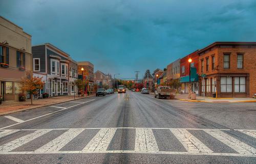 A quiet street scene with shops on either side, under a cloudy sky, and a crosswalk in the foreground.