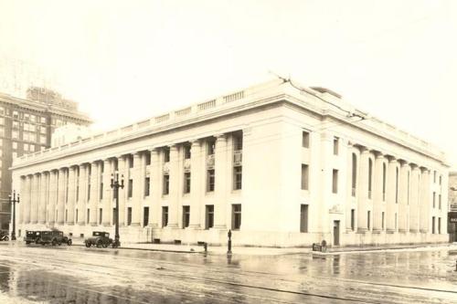 Historic building with columns, captured in black and white, reflecting a rainy street scene with vintage cars.