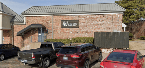 A brick building with a sign reading "Tip the Griffin" and parked cars in front.