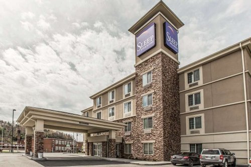 Exterior view of a Sleep Inn hotel with a stone facade and a large sign, under a cloudy sky.