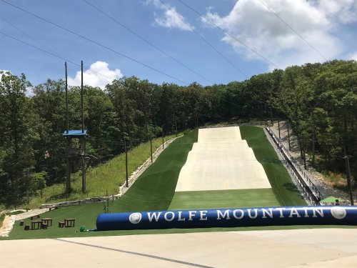 A ski slope at Wolfe Mountain, surrounded by trees, with a blue banner and clear skies above.