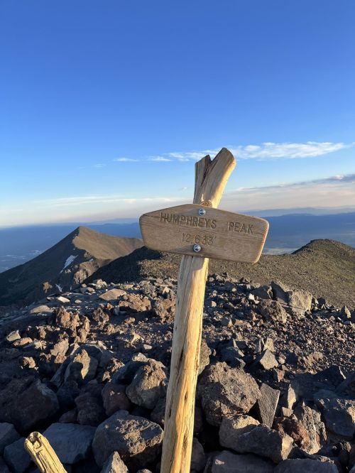 Signpost marking Humphreys Peak at 12,633 feet, with rocky terrain and a clear blue sky in the background.
