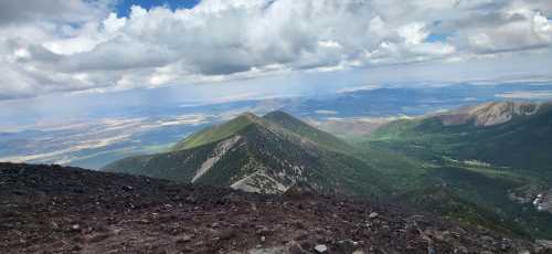 A panoramic view of green mountains under a partly cloudy sky, with valleys stretching into the distance.