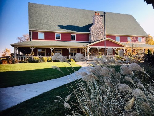 A large red and gray house with a stone chimney, surrounded by green grass and ornamental grasses in the foreground.