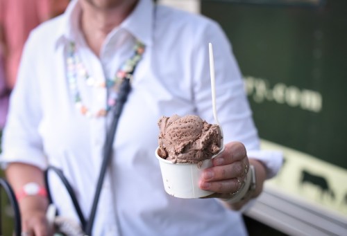 A person holding a cup of chocolate ice cream with a spoon, wearing a white shirt and a colorful necklace.