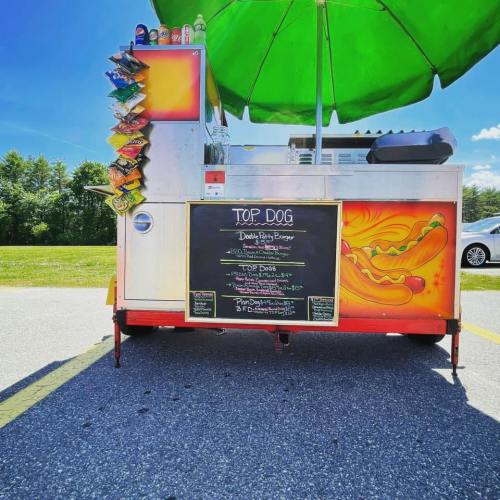A colorful food cart named "Top Dog" with a menu featuring hot dogs and burgers, shaded by a green umbrella.