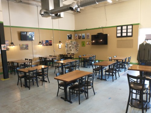 A spacious dining area with wooden tables and chairs, featuring wall art and TVs, in a well-lit setting.