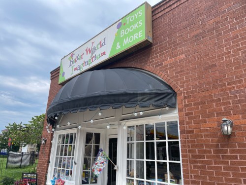 Exterior of a brick building with a sign reading "Toy World" and a black awning, featuring toys, books, and more.