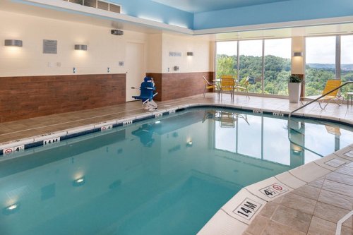 Indoor swimming pool with lounge chairs, large windows, and scenic views of greenery outside.