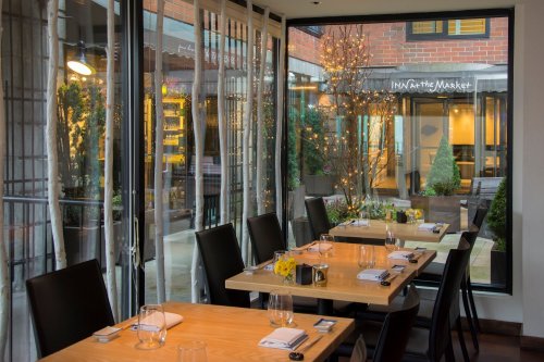 A cozy restaurant interior with wooden tables, black chairs, and a view of a decorated outdoor space.