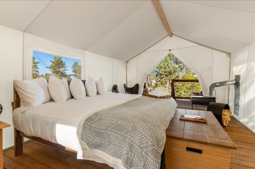 Cozy glamping tent interior with a bed, pillows, and a wooden table, surrounded by nature.