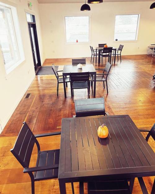 A bright, modern room with wooden floors, featuring several black tables and chairs, and a small pumpkin centerpiece.