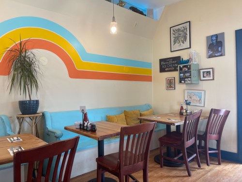 Cozy restaurant interior with colorful wall art, wooden tables, and a blue couch adorned with yellow cushions.
