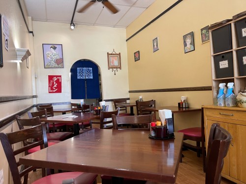 Cozy restaurant interior with wooden tables, chairs, and artwork on the walls, featuring a blue fabric hanging.