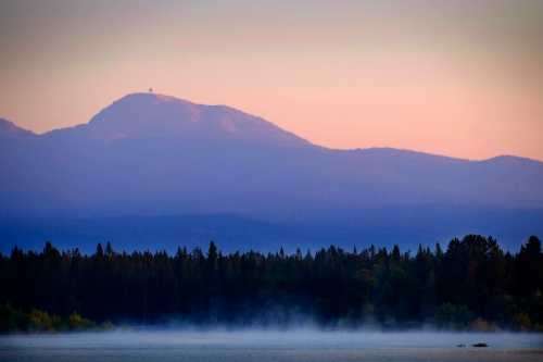 A serene landscape featuring a misty lake with mountains in the background under a soft, pastel sky.