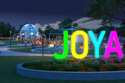 Colorful "JOYA" sign in a vibrant park at night, featuring illuminated playground equipment and lush greenery.