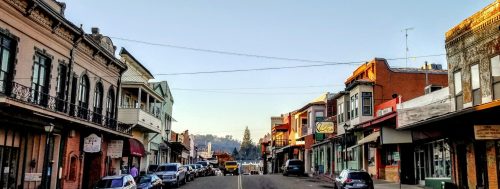 A charming street lined with historic buildings and parked cars, under a clear blue sky.