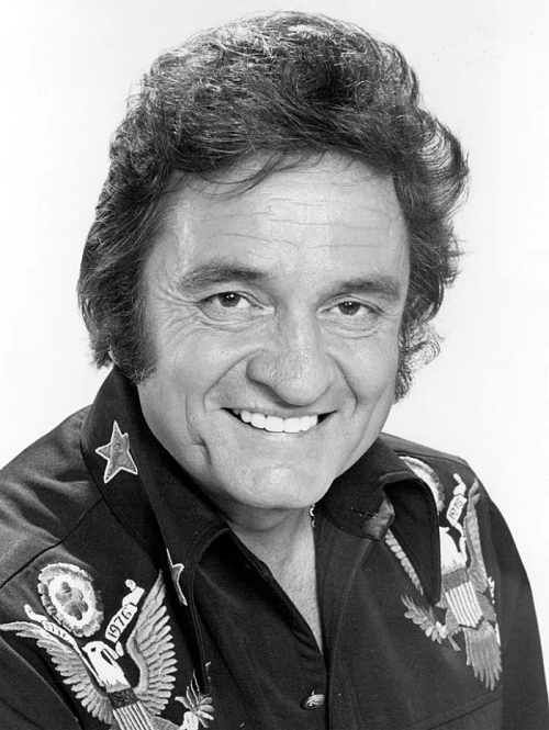 Black and white portrait of a smiling man with dark hair, wearing a shirt with embroidered eagle designs.